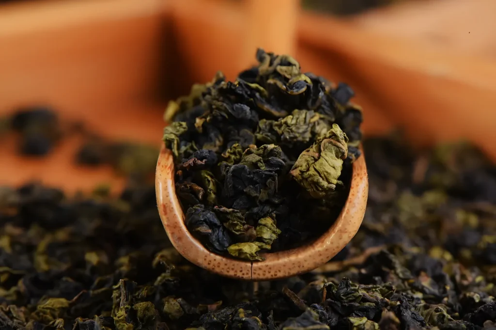 A wooden scoop filled with dried loose tea leaves, with more leaves scattered in the background.