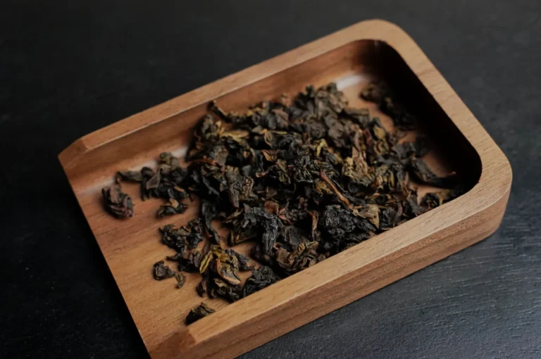 A wooden tray containing loose dried tea leaves.