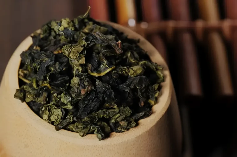 A wooden bowl filled with dried green tea leaves.