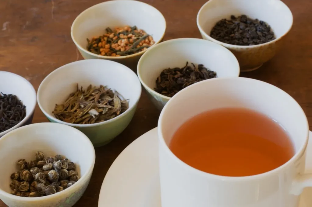 A cup of tea surrounded by small bowls of different types of tea leaves.