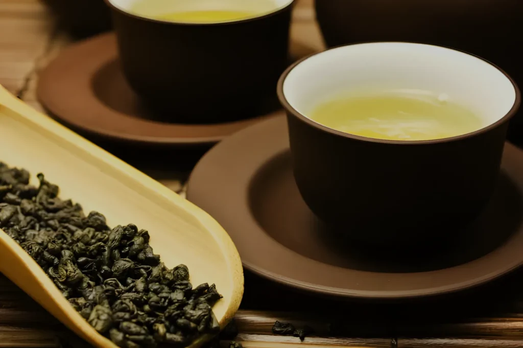 A close-up of two cups of tea on saucers, accompanied by a bamboo dish of loose tea leaves.
