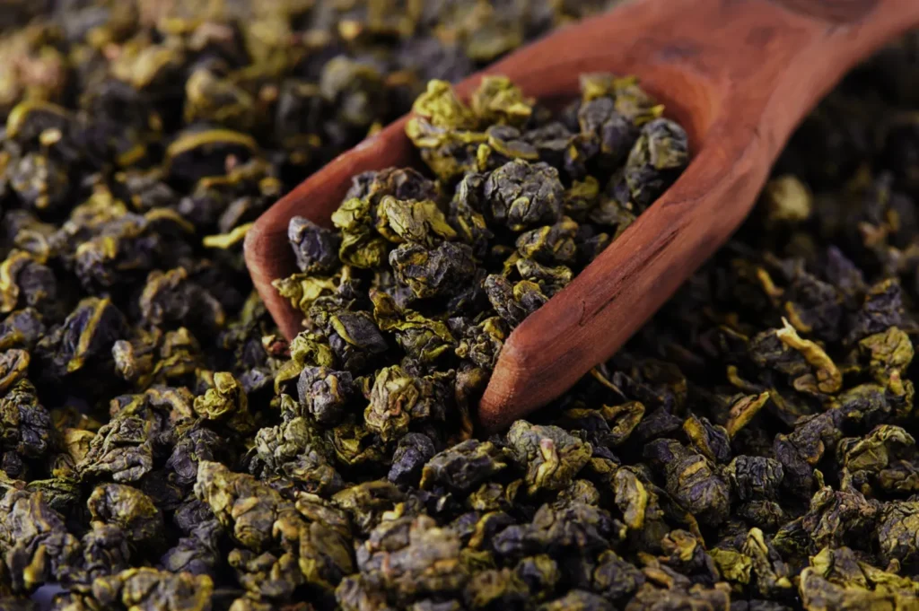 Dried oolong tea leaves with a wooden scoop.