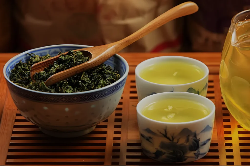 A bowl of loose green tea leaves with a wooden spoon, two cups of freshly brewed green tea, and a glass of tea, all placed on a bamboo tray.