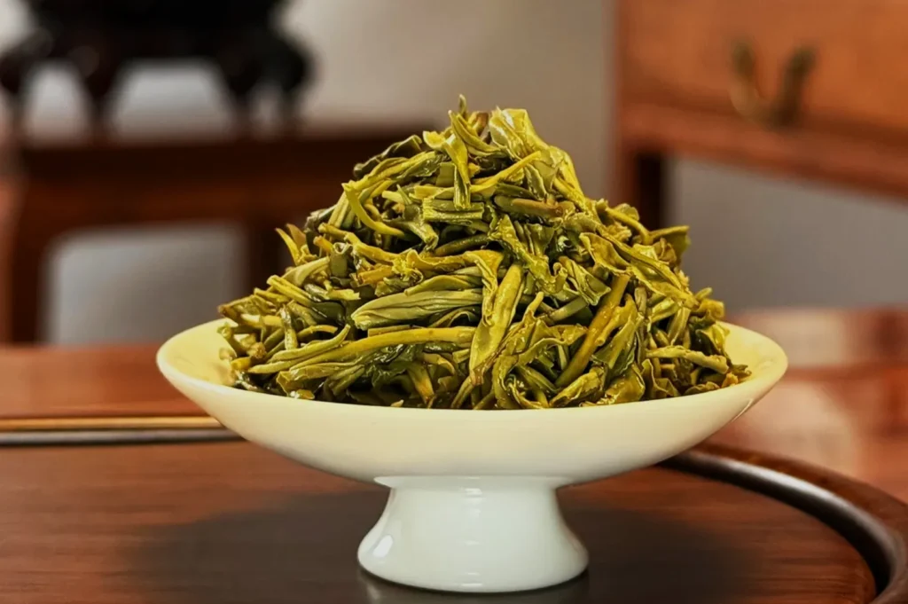 A bowl of green tea leaves on a wooden table.