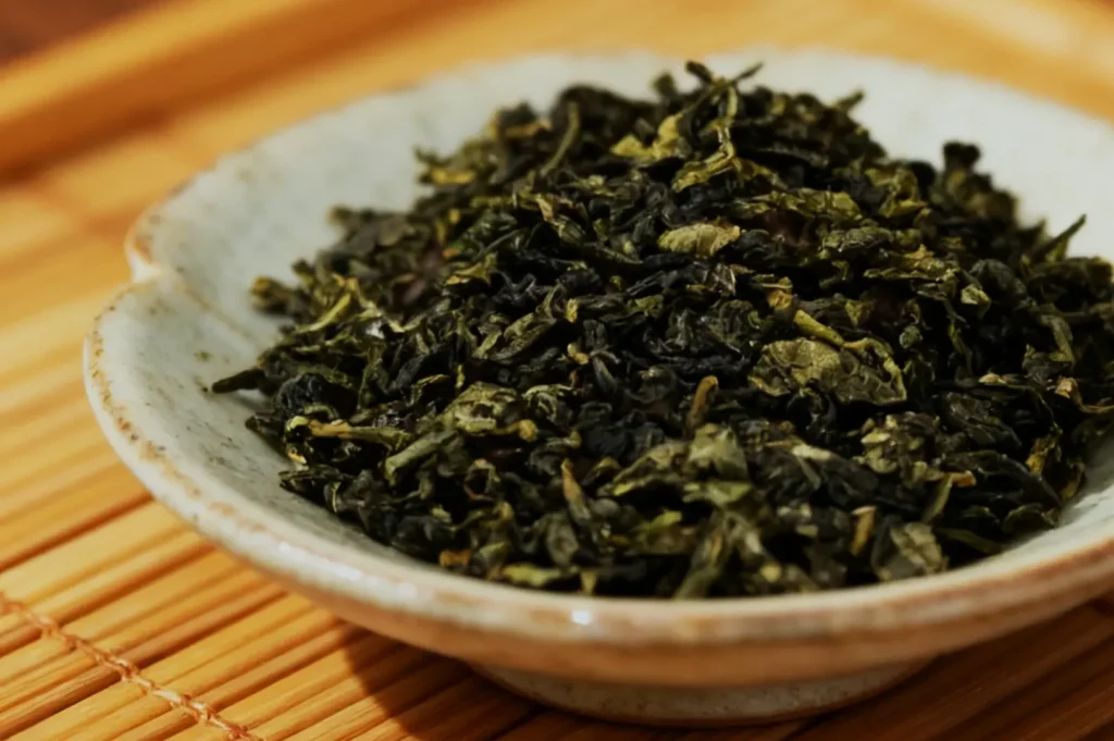 Dried green tea leaves in a small ceramic bowl on a bamboo mat.
