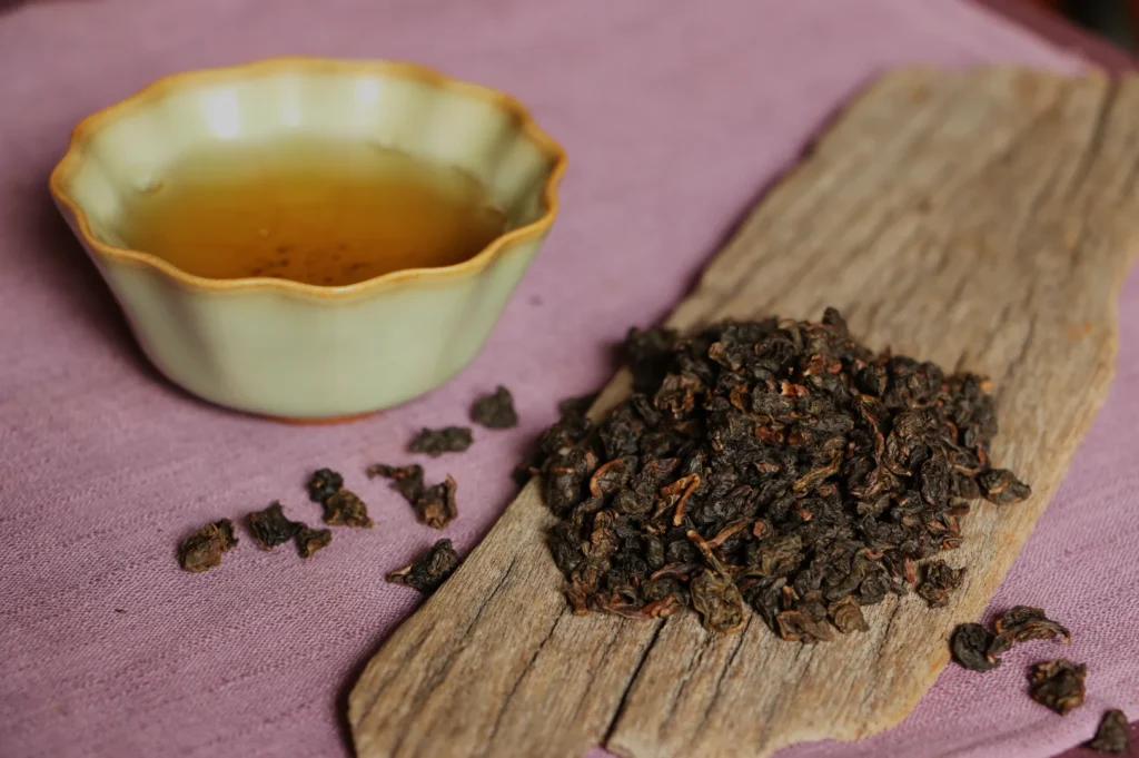 A bowl of brewed tea next to loose tea leaves on a piece of wood.