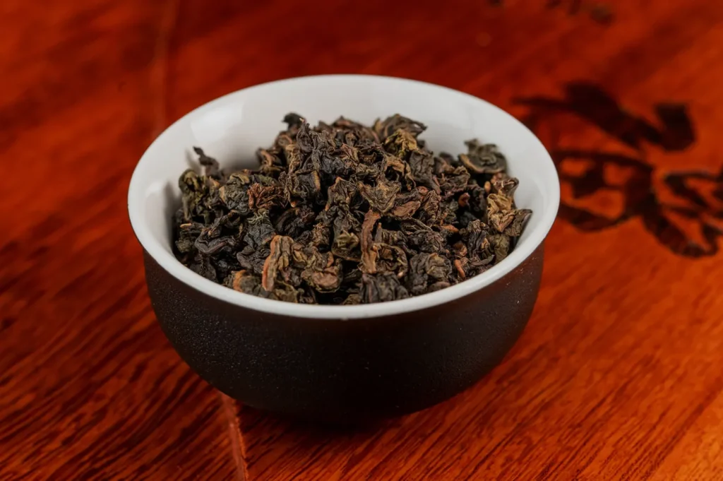 A small black bowl filled with loose tea leaves on a wooden surface.