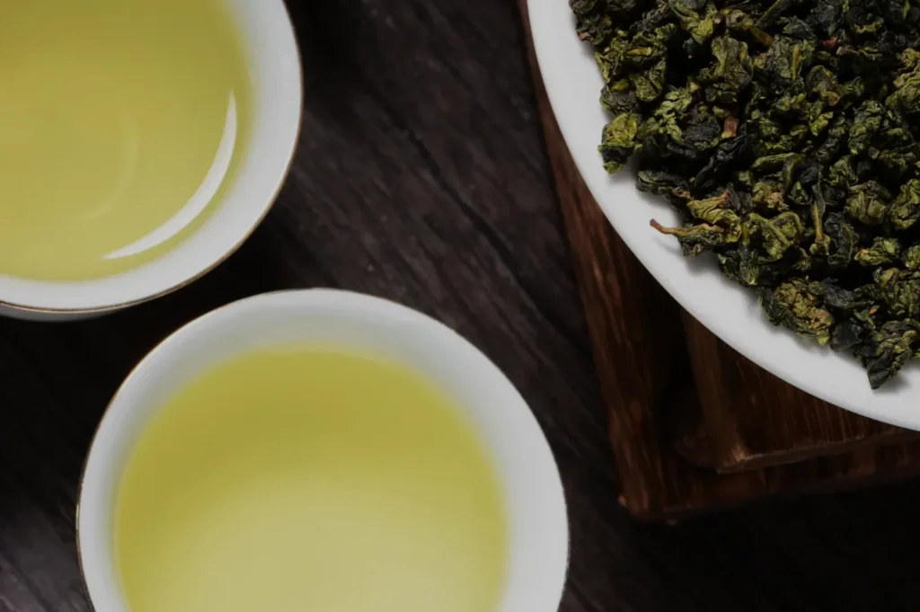Aerial view of two cups of brewed oolong tea next to a small bowl of dry oolong tea leaves.