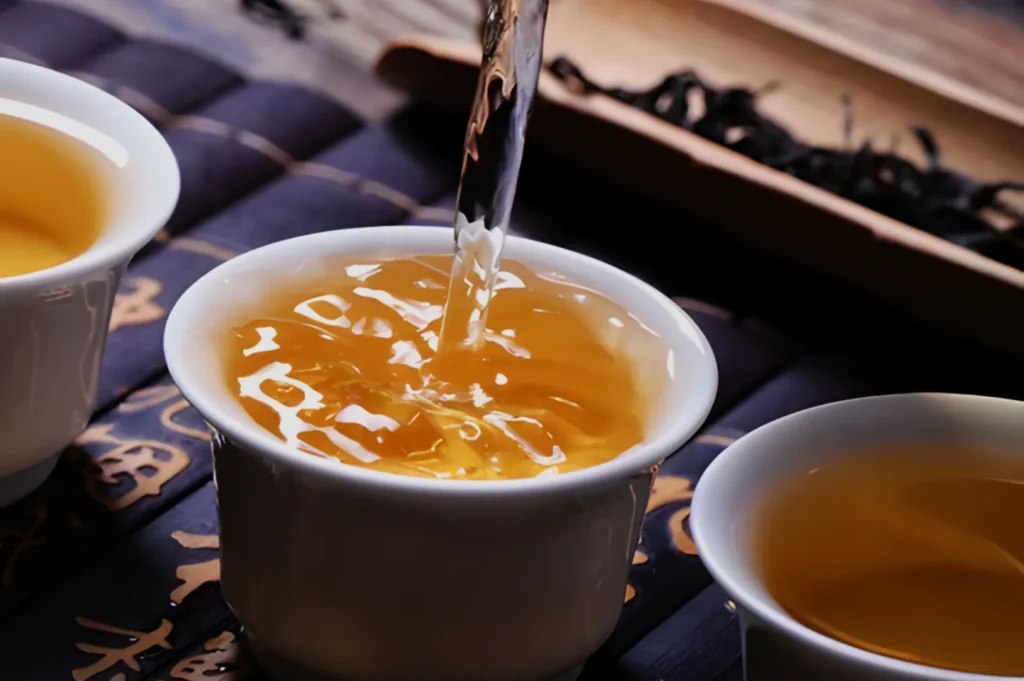 A close-up of tea being poured into white cups, with a dark background featuring loose tea leaves.