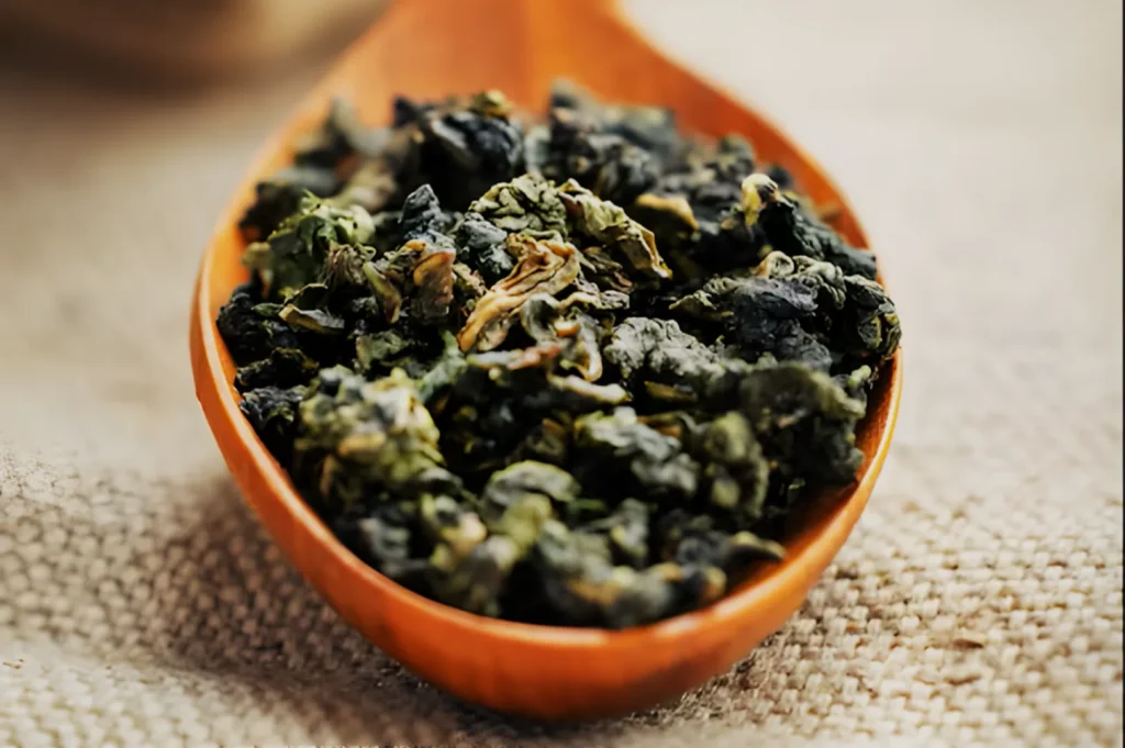 A wooden spoon holding loose dried green tea leaves.