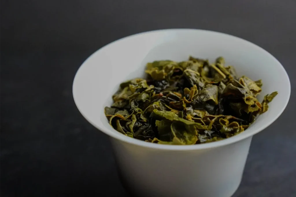 White ceramic cup filled with loose dried herbal tea leaves and petals, set against a dark background, creating a calm, rustic mood.