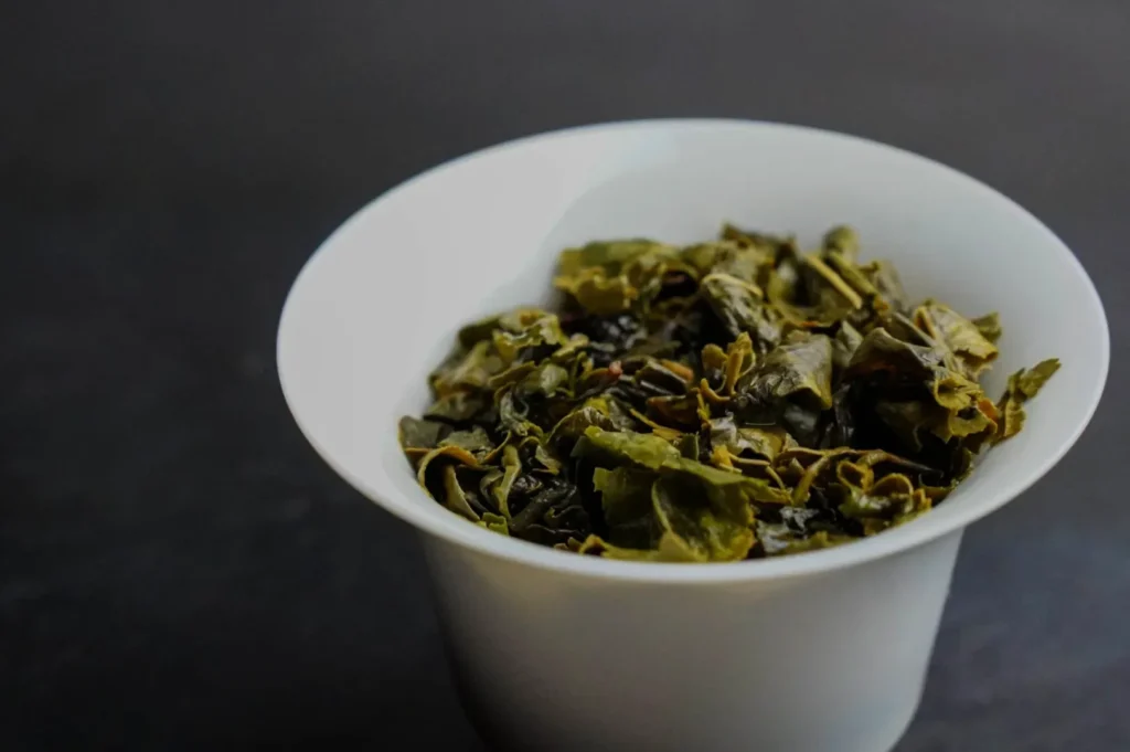 A white bowl filled with dried green tea leaves.