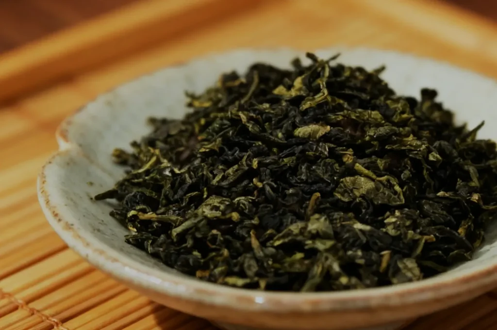 A shallow bowl filled with dried green tea leaves.