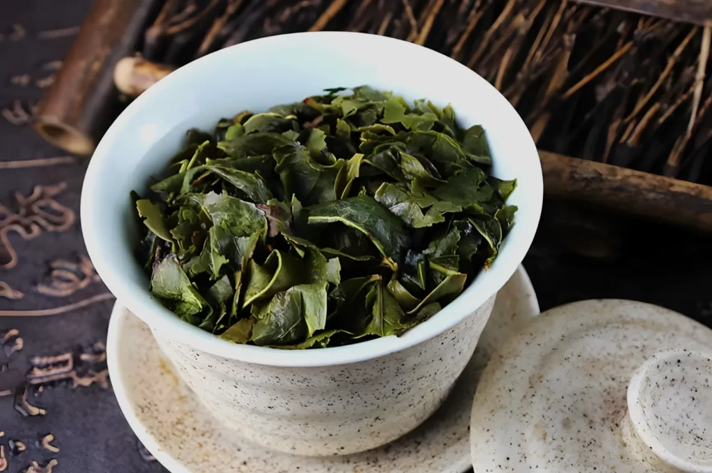 A bowl of dried green tea leaves on a textured background.