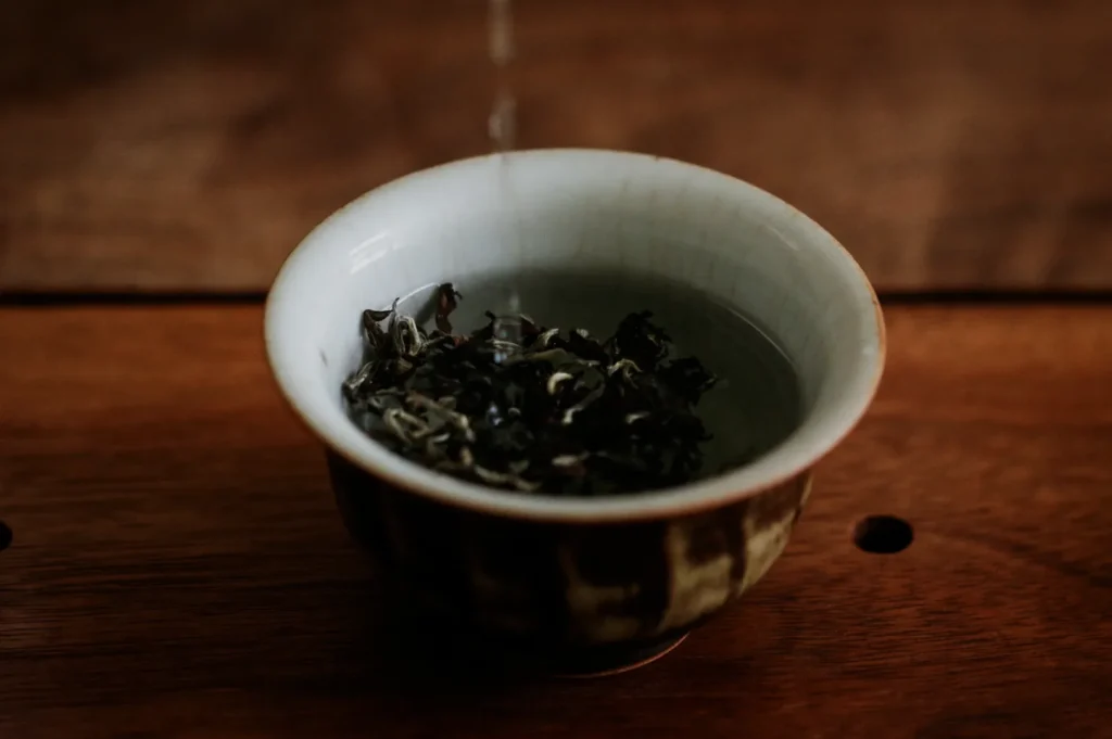 A small bowl filled with water and dried tea leaves, placed on a wooden surface.