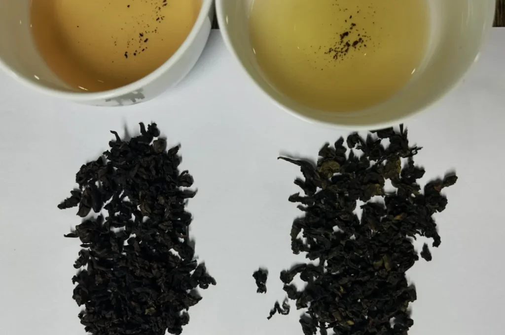 Two cups of tea with different colors beside dried tea leaves.