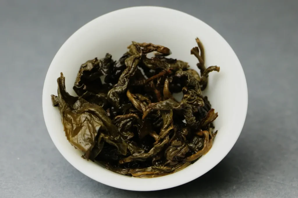 A small white bowl filled with dark, curled dried tea leaves.