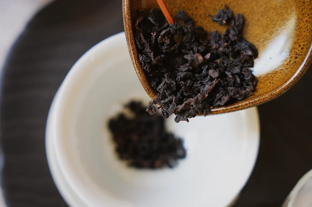 A scoop of dried tea leaves being poured into a white bowl from a brown serving dish.