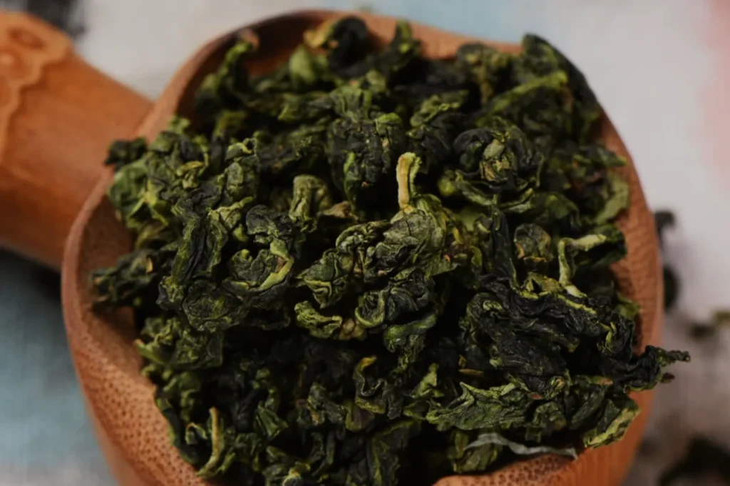 Dried green tea leaves in a wooden bowl.