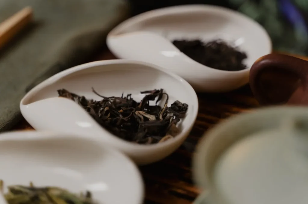 Three white ceramic dishes containing different types of loose tea leaves.