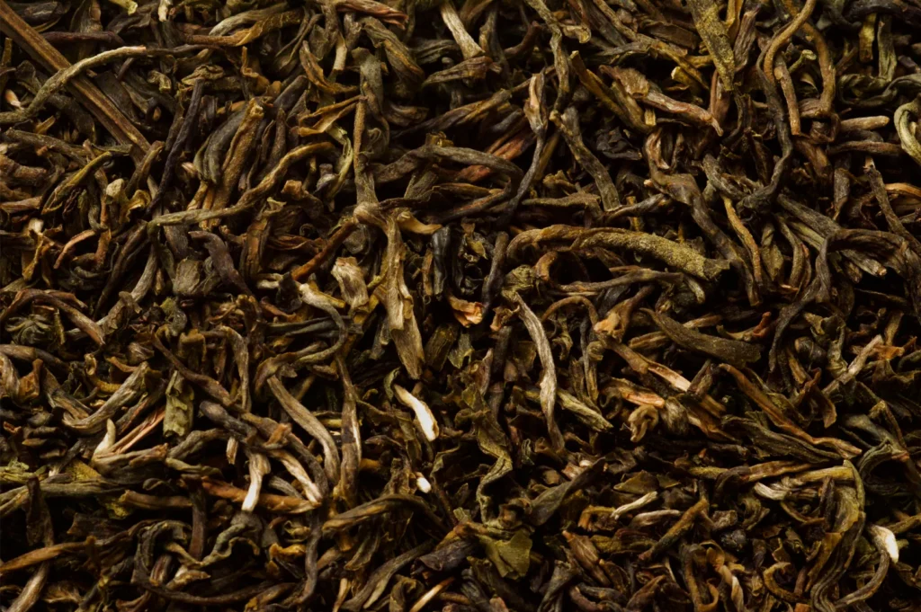 A close-up of dried, twisted tea leaves in deep brown and golden tones, their tangled texture filling the frame with an earthy, rustic feel.