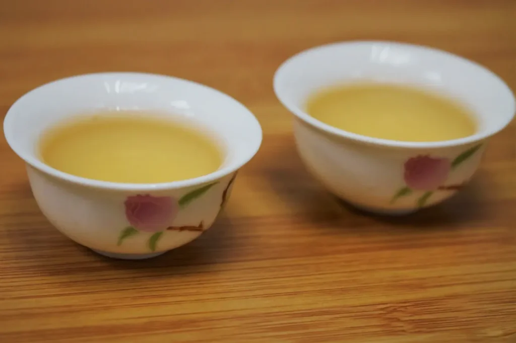 Two white porcelain teacups with pink floral patterns hold golden tea on a wooden table, creating a warm, calm, inviting scene.