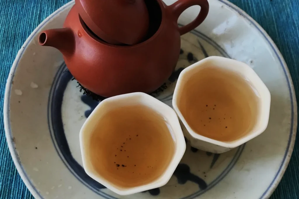 A reddish-brown clay teapot and two small white cups of amber tea rest on a patterned ceramic tray, creating a calm, intimate tea setting.