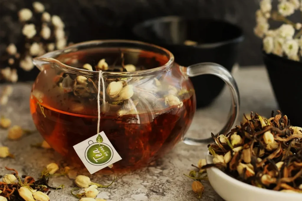 Glass teapot of amber herbal tea with a green tea tag, surrounded by dried flowers and botanicals; warm, rustic styling evokes a calm tea ritual.