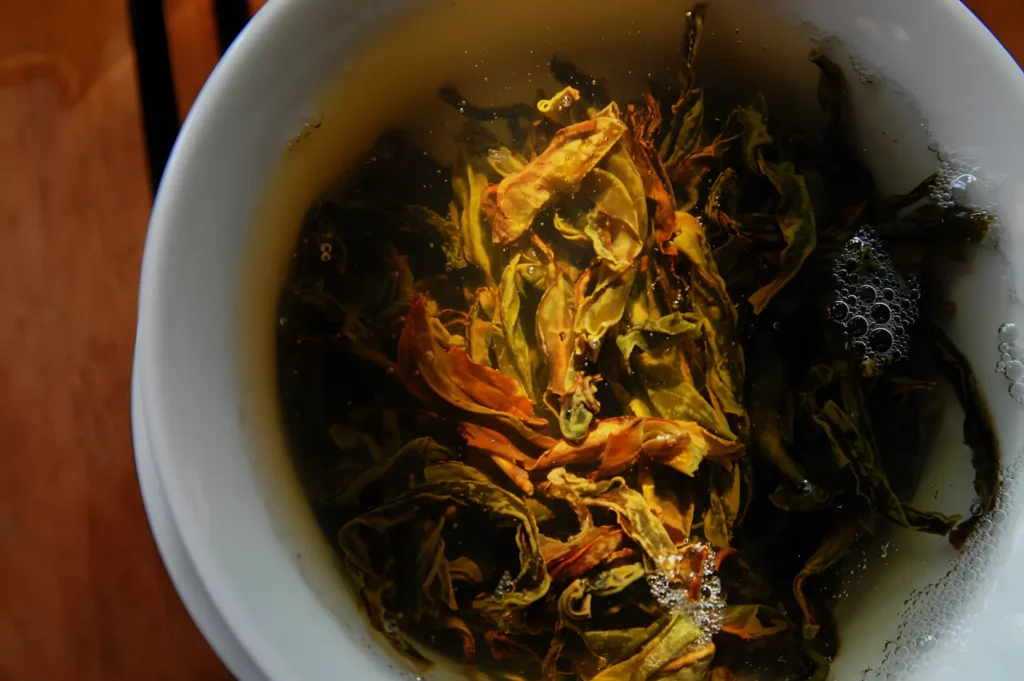 Close-up of dried tea leaves steeping in a white cup, their golden-brown and green colors glowing in warm light, creating a rich, soothing mood.